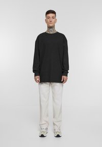 Svart langermet t-skjorte med avslappet passform, rund hals, og ribbestrikkede mansjetter, kombinert med beige vide bukser og grå sneakers.