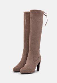 Bottes hautes en daim marron jusqu'aux genoux, de forme effilée, avec un bout pointu et un talon haut. Elles comportent une fermeture à nouer en haut pour un ajustement.