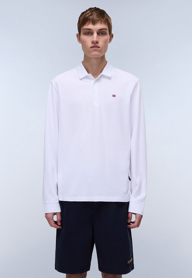 Vit långärmad pikétröja med knäppning med två knappar och en liten logotyp. Kombinerad med mörka shorts, som har en strukturerad tyg och en avslappnad passform.