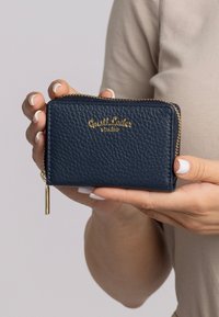 Navy blue leather wallet with a textured finish, gold branding, and a zip closure. Features a tassel detail on the zipper pull.