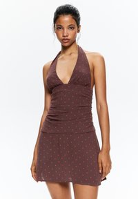 Robe halter brune à pois rouges, avec un décolleté en V profond et des détails froncés sur le buste et la jupe. Tissu léger.