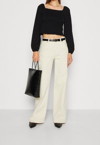 Top nero corto con maniche lunghe a sbuffo, pantaloni beige a gamba larga, borsa nera in pelle sintetica e tacchi neri a punta. Dettaglio scollo quadrato.