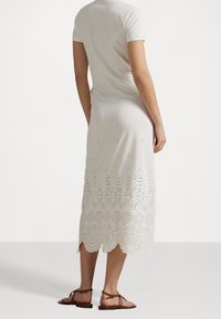 Biała bawełniana sukienka z falbaniastym dołem i detalami z ażurowym wzorem. Dopasowany fason z krótkimi rękawami. Noszona z brązowymi płaskimi sandałami.