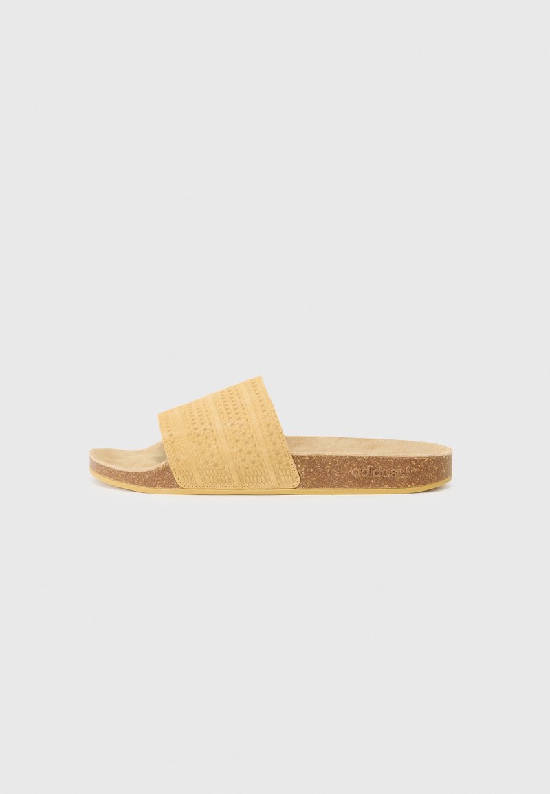 Gule slip-on sandaler med en teksturert stoffrem, korkfotseng og flat gummisåle. Merkbar merkevarelogo på siden.