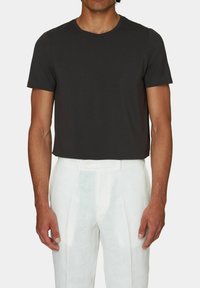 T-shirt in cotone nero con scollatura tonda classica, maniche corte e vestibilità comoda, abbinata a pantaloni in lino bianchi plissettati.