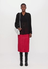 Camicia nera trasparente con bottoni e maniche lunghe, abbinata a una gonna midi in pelle rossa e stivali neri alti fino al ginocchio. Accentata da una borsa argentata.