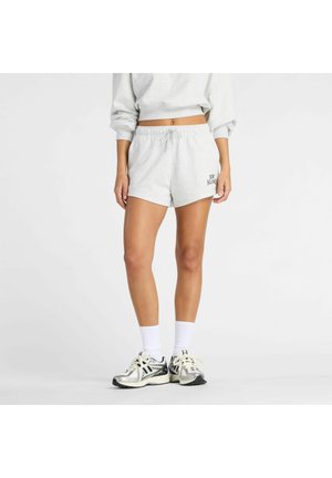 Person iført lysegrå New Balance-shorts, hvide sokker og sølvfarvede løbesko, stående mod en ensartet hvid baggrund.
