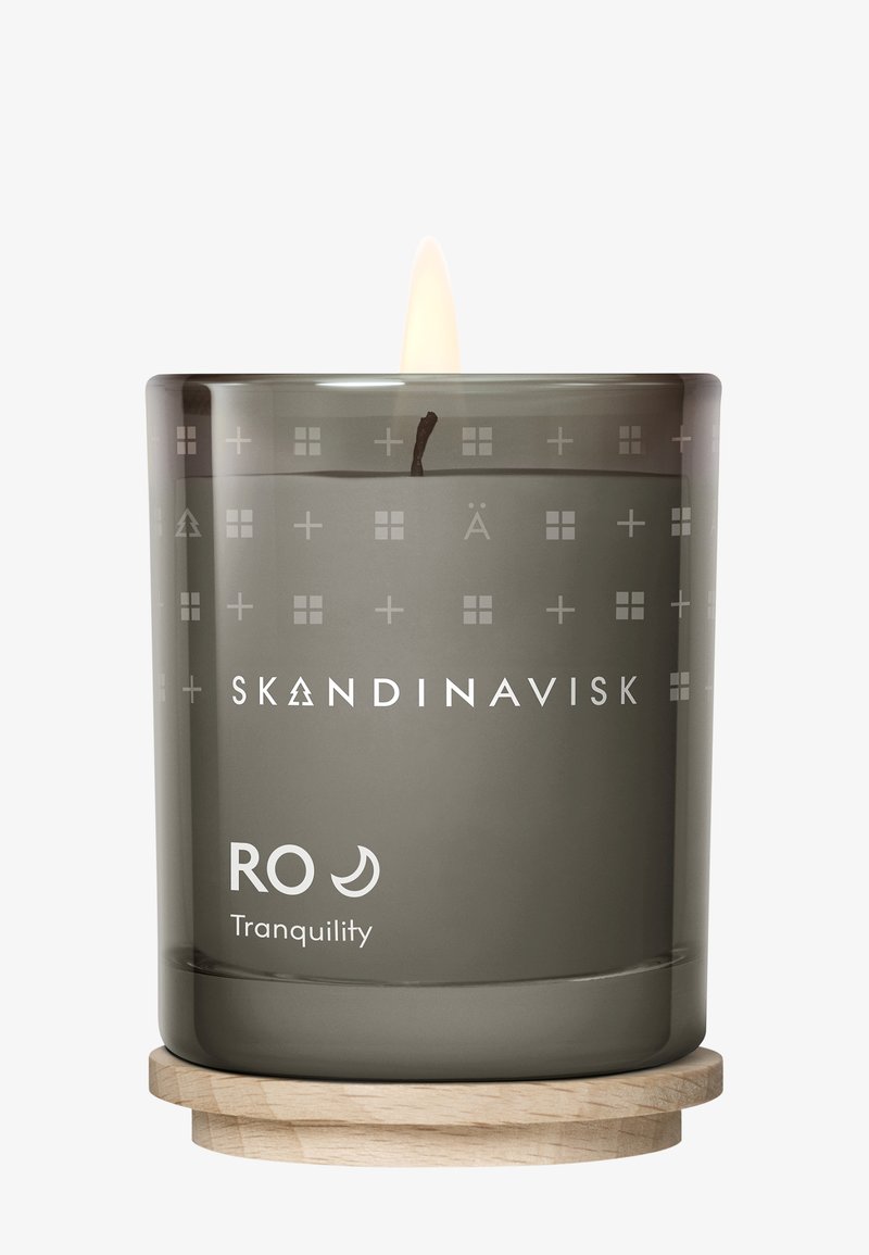 Bougie parfumée dans un photophore en verre gris givré avec des motifs gravés. Base en bois soutient le verre. L'étiquette porte les inscriptions « Skandinavisk » et « RO Tranquility ».