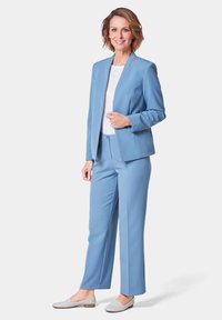 Lichtblauw pak gemaakt van soepel materiaal, met een getailleerde blazer en wijde broekspijpen. Gepaarde met een wit shirt en grijze instappers.