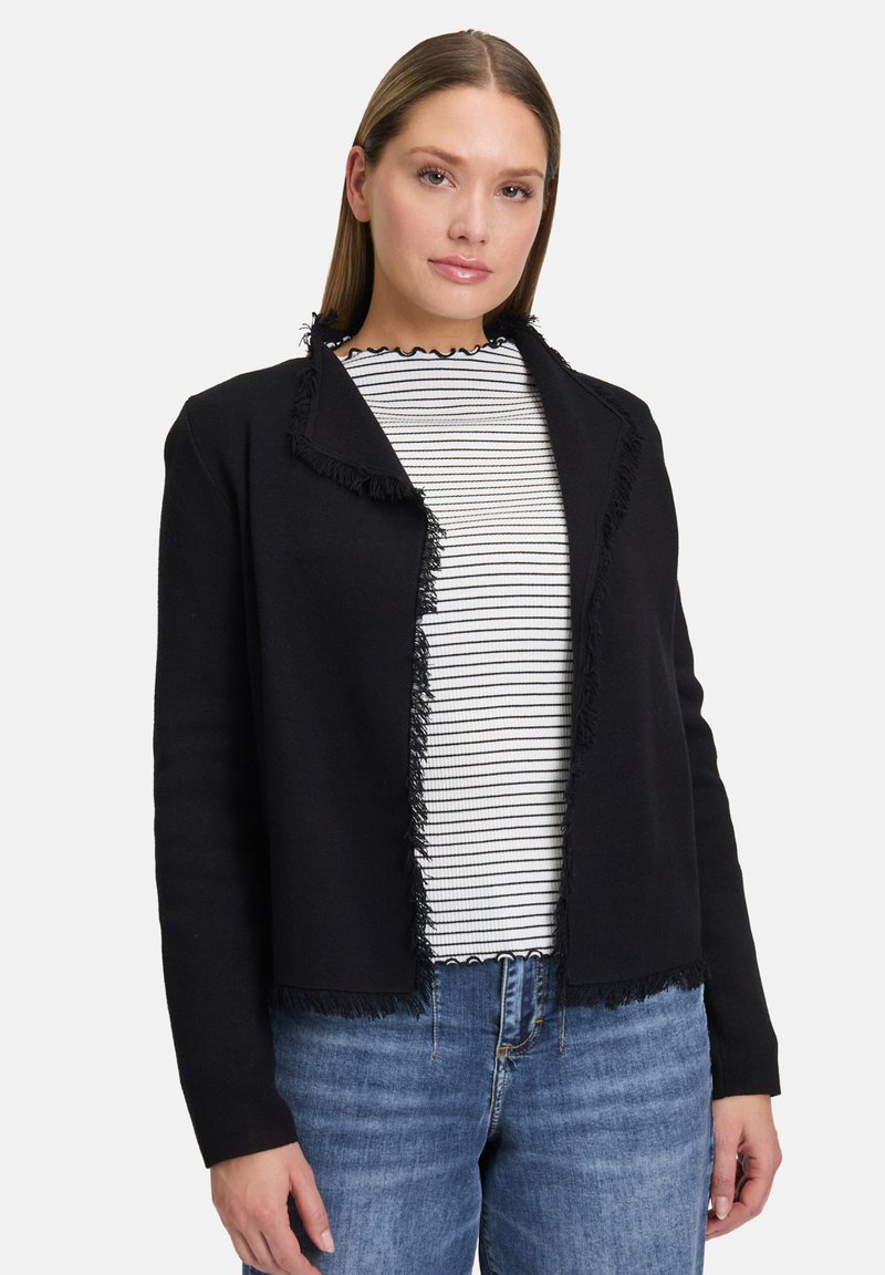 Černý kardigan s třásněmi a texturovaným povrchem, s otevřeným předním dílem a dlouhými rukávy, přeložený přes černo-bílé pruhované tričko.