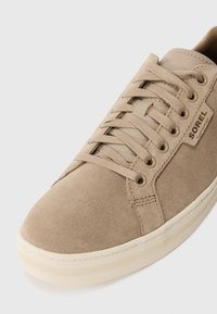 Zapatilla de ante beige con cordones planos, puntera redondeada y suela de goma texturizada. Presenta una pequeña etiqueta de marca en el lateral.
