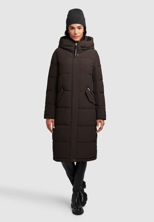 Pikk, tumepruun puffer-jakk, millel on kapuuts ja suured eespool asuvad taskud. Sile tekstuur, tikitud disain ja eesmine lukustus. Kantud halli beanie'iga.