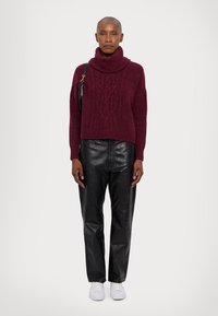 Bordo turtleneck pulover z kabelskim pletenjem, v kombinaciji z črnimi usnjenimi hlačami in belimi supergami. Enostavna torba na rami.