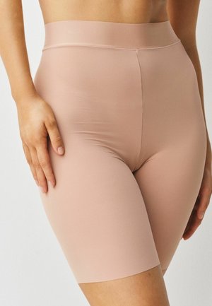 Woman wearing high-waisted, seamless, nude-colored shaping shorts with a ribbed texture, hand resting on thigh.