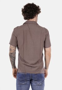 Camicetta corta marrone con una vestibilità rilassata, caratterizzata da una morbida texture e dettagli di cucitura delicati sul retro. Abbinate a jeans blu.