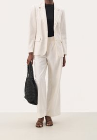 Blazer et pantalon à fines rayures claires en tissu lisse, assortis à un haut noir ajusté et un sac fourre-tout noir en tissu tissé.