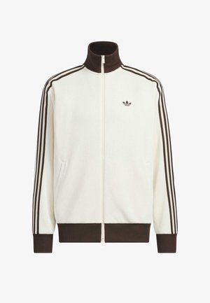 White zip-up track jacket with brown ribbed collar, cuffs, and hem, featuring three brown stripes down sleeves and small logo on chest.