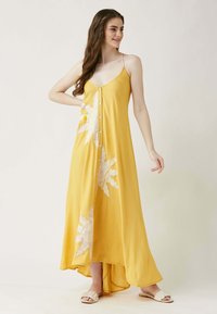 Gelbes Maxikleid mit Spaghetti-Trägern, das ein dekoratives Blumenmuster, Knopfdetails und ein asymmetrisches Saumdesign aufweist. Glatter Stoff und lockere Passform.