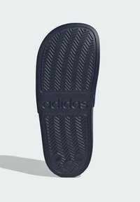 Suela de goma negra con patrón de espiga; cuenta con el logo 'adidas' en relieve y marcas de tamaño; textura suave, forma redondeada.