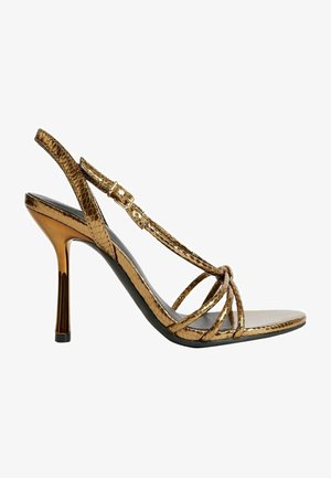 Sandały na wysokim obcasie z paskami w metalizowanym złotym kolorze imitującym węża, o smukłym designie, z odkrytymi palcami i paskiem na kostkę z klamrą w złotym odcieniu.