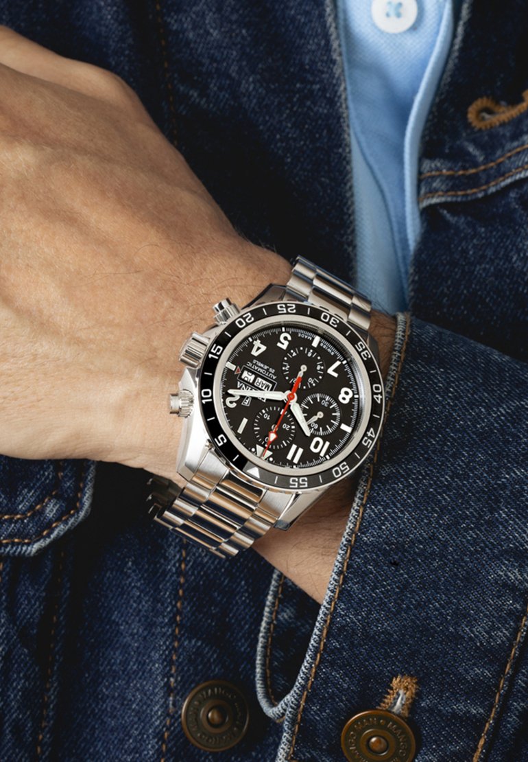 Orologio in acciaio inox argentato con quadrante nero, indici bianchi, funzioni cronografo e bracciale in metallo, posato su una mano.