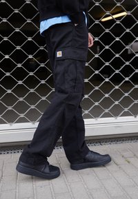 Schwarze Cargo-Hosen aus robustem Material, mit Seitentaschen und einem Carhartt-Logo-Patch. Kombiniere sie mit mattschwarzen Sneakers.