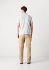 Camisa polo cinza claro com mangas curtas, combinada com calças bege. O tecido parece suave e leve. Sapatos castanhos e um design simples.