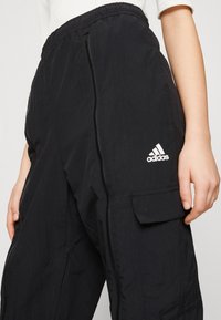 Svarta cargobyxor med elastiskt midjeband, sidogångjärn och en ficka. Har en vit Adidas-logotyp på nederbenet. Lättviktig tyg.