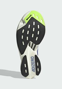 Batų pado juodi guminiai sukibimo raštai, balta vidurinė dalis ir žalia akcentas šalia kulno. Ant šono matoma "ADIZERO" prekės ženklas.