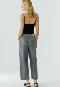 Schwarzes Tanktop mit dünnen Trägern, kombiniert mit grauen, hoch taillierten, weit geschnittenen Jeans aus Denim, die über Taschen auf der Rückseite und subtile Nähtdetails verfügen.