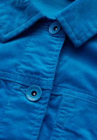 Blå kordflorsmaterial med en texturerad yta, med en knappstängning och krage, som visar en slät finish och en livfull färg.