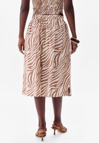 Jupe à motifs zèbre marron et beige, design plissé, mi-longue, avec une taille noire et une étiquette sur le côté. Portée avec des sandales à talons marron.