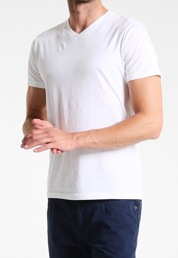 Man wearing plain white short-sleeve V-neck T-shirt and dark blue pants, standing with hands clasped in front.