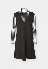 Robe noire sans manches avec un profond décolleté en V, portée avec un col roulé à manches longues rayé noir et blanc en dessous. Tissu lisse, design décontracté.
