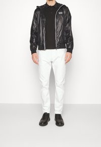 Svart, zip-up, huva jacka med en glansig finish, parat med en svart polo skjorta och vita byxor, komplett med svarta sneakers.