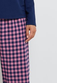 Haut à manches longues bleu marine associé à un pantalon de pyjama à carreaux roses et bleu marine. Le pantalon dispose d'un tissu doux et texturé ainsi que d'une coupe large et décontractée.