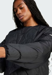 Černá péřová bunda s vysokým límcem, zipovým zapínáním a vroubkovanými manžetami. Látka má hladký povrch s prošitými detaily.