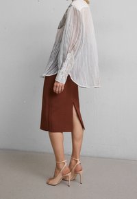 Vit genomskinlig randig skjorta, brun mittlång kjol med sidoklyfta, och nude högklackade sandaler, som framhäver lager på lager-texturer och eleganta linjer.