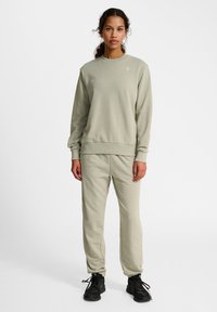Lichtgroene sweatshirt en bijpassende joggers, gemaakt van zachte stof, met een ronde hals en ribgebreide manchetten. Draag met zwarte sneakers.