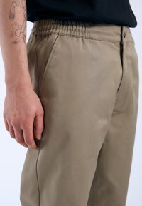Beige broek met een soepele textuur, elastische tailleband en een zijzak. Geverfde details en een klassieke pasvorm.