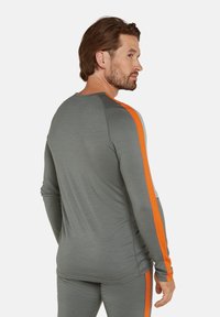 Långärmad sporttröja i grått tyg med orange och ljusblå accentsträck längs axlarna. Har rundad halslinning och slimmad design.