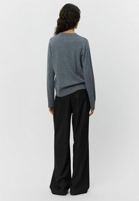 Maglione grigio con colletto a giro e orlo a coste, abbinato a pantaloni neri a gamba larga con un sottile motivo verticale.