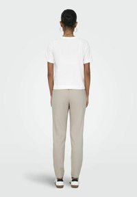 T-shirt blanc à manches courtes, au design court, associé à un pantalon beige sur mesure, porté avec des baskets noir et blanc, vu de dos.