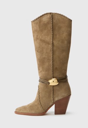 Hohe, sandfarbene Wildlederstiefel mit einem Holz-Blockabsatz, geflochtenem Besatz und gewickelten Lederbändern mit einer goldenen ovalen Schnalle.