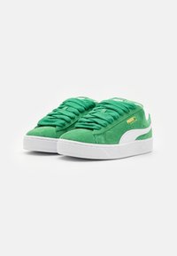 Grønne semskede sneakers med hvite detaljer og teksturerte gummisåler. Har tykke lisser og et PUMA-logo i gull. Lavt design.