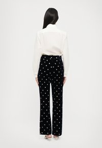 Námořnické sametové kalhoty s vykrojeným designem, zdobené malými květinovými vzory. Kombinované s bílou košilí s dlouhým rukávem, pohled zezadu.