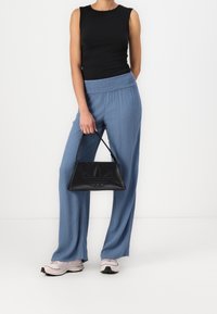 Svart utanärmad topp, ljusblå vida byxor med elastisk midja, håller en liten svart handväska med präglad logotyp och texturerad detalj.