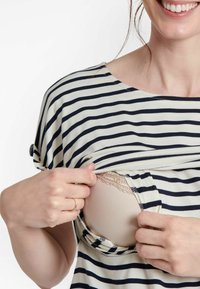 Maglietta a righe in crema e blu navy, con scollo rotondo e maniche corte, con un'apertura che rivela un reggiseno color carne rifinito in pizzo sottostante.