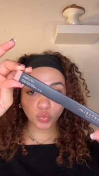 Czarne opakowanie konturówki do ust o matowym wykończeniu, z białym napisem. Produkt jest trzymany pionowo w dłoni osoby.