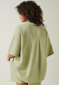 Camicia oversize verde oliva con maniche corte, spallina sul retro e un tessuto morbido e texture, dal taglio rilassato.